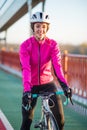 Portrait of Young Smiling Female Cyclist in Pink Jacket Resting with Road Bicycle in the Cold Sunny Autumn Day