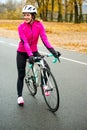 Portrait of Young Smiling Female Cyclist in Pink Jacket Resting with Road Bicycle in the Cold Sunny Autumn Day