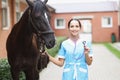 Portrait of young smiling female veterinarian holding steepler while standing next to horse Royalty Free Stock Photo
