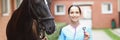 Portrait of young smiling female veterinarian holding steepler while standing next to horse Royalty Free Stock Photo