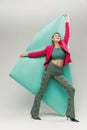 Portrait of young smiling girl in bright jacket and vintage pants posing with paper piece isolated over grey studio Royalty Free Stock Photo