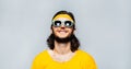 Portrait of young smiling guy with long hair; wearing sunglasses, yellow shirt and band on head. Background of grey textured wall. Royalty Free Stock Photo