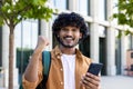 Portrait of a young smiling handsome Indian man standing on the street with a phone in his hands and rejoicing in Royalty Free Stock Photo