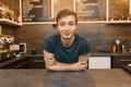 Portrait of young smiling male barista with arms crossed standing behind cafe counter. Coffee shop business concept Royalty Free Stock Photo