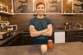 Portrait of young smiling male barista with prepared drink with arms crossed standing behind cafe counter. Coffee shop business co Royalty Free Stock Photo