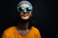 Portrait of young smiling man on black background, wearing blue sunglasses and orange shirt. Royalty Free Stock Photo