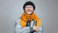 Portrait of young smiling man with knitted orange scarf, wearing glasses, black beanie hat and grey bomber. Royalty Free Stock Photo