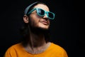 Portrait of young smiling man, wearing blue sunglasses and grey hat on black background. Royalty Free Stock Photo