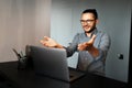 Portrait of young smiling man working home at laptop, feels happy about work, showing hands on screen, wearing eyeglasses. Royalty Free Stock Photo
