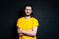 Portrait of young smiling man in yellow shirt on background of black brick wall. Royalty Free Stock Photo