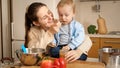 Portrait of young smiling mother feeding her baby son with fruit puree on kitchen. Concept of little chef, children Royalty Free Stock Photo