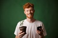 Portrait of young smiling redhead bearded young man, holding spotted plant and mobile phone