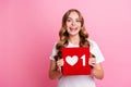 Portrait of young smiling very optimistic blogging girl in white t shirt holding red like symbol repost isolated on pink