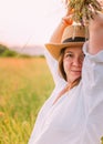 Portrait of young smiling woman dressed in light summer clothes and straw hat walking by high green grass meadow with wildflowers Royalty Free Stock Photo