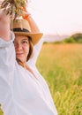 Portrait of young smiling woman dressed in light summer clothes and straw hat walking by high green grass meadow with wildflowers Royalty Free Stock Photo