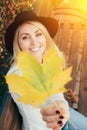 Portrait of a young smiling woman holding yellow maple leaf agains her face, wearing white sweater and black felt hat. Royalty Free Stock Photo