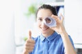 Portrait of a young smiling woman holds thumbs up and looks into pipe made of paper