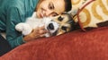 Portrait of young smiling woman hugging pet. Cute Welsh Corgi puppy resting with owner, spending time together at home.