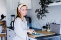 Portrait of young smiling woman with pink clay facial mask cutting cucumber for salad on the kitchen. Every day home Royalty Free Stock Photo