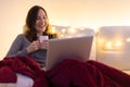 Portrait of young smiling woman sitting on sofa with laptop and cup of coffee or tea and looking on the screen Royalty Free Stock Photo