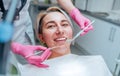 Portrait of young smiling woman sitting in stomatology clinic chair and doctor\'s hands with dental Mouth mirror and Dental