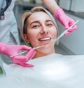 Portrait of young smiling woman sitting in stomatology clinic chair and doctor\'s hands with dental Mouth mirror and Dental