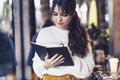 Portrait of young smiling woman standing in cafe near window, writing in notebook. Girl writes notes diary, makes business plan Royalty Free Stock Photo