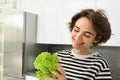 Portrait of young smiling woman, vegetarian washing lettuce leaves for salad, holding ingredients in hand, making a Royalty Free Stock Photo