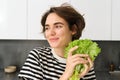 Portrait of young smiling woman, vegetarian washing lettuce leaves for salad, holding ingredients in hand, making a Royalty Free Stock Photo