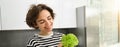 Portrait of young smiling woman, vegetarian washing lettuce leaves for salad, holding ingredients in hand, making a Royalty Free Stock Photo