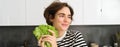 Portrait of young smiling woman, vegetarian washing lettuce leaves for salad, holding ingredients in hand, making a Royalty Free Stock Photo