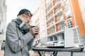 Portrait of young smiling woman in warm clothes, knitted hat. Girl warming her hands with cup of hot drink in an outdoor cafe on Royalty Free Stock Photo