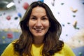 Portrait of young smiling woman in yellow t-shirt standing with bouldering, climbing wall behind