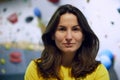 Portrait of young smiling woman in yellow t-shirt standing with bouldering, climbing wall behind