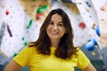 Portrait of young smiling woman in yellow t-shirt standing with bouldering, climbing wall behind