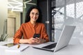 Portrait of a young Spanish business woman working in the office at the laptop, using the phone, smiling at the camera Royalty Free Stock Photo
