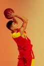 Portrait of young sportive man, basketball player throwing ball into basket  over orange studio background in Royalty Free Stock Photo