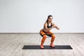 Portrait of young sporty healthy beautiful woman in black top and orange leggings doing squatting with elastic resistance band Royalty Free Stock Photo