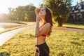 Portrait of young sporty woman in black and pink top and black shorts standing on green lawn at sunrise in sunny day.