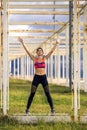 Portrait of young and sporty woman in sportswear standing with raised up hands.