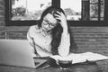 Portrait of young stressed businesswoman sitting at office desk in front of laptop, touching head with tired facial expression. Royalty Free Stock Photo