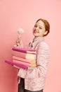 Portrait of young student, girl wearing uniform, holding books looking at camera and smiling over pink studio background Royalty Free Stock Photo