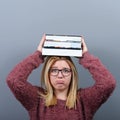 Portrait of a young student woman holding books on head against gray background.Tired of learning/studying concept