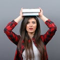 Portrait of a young student woman holding books on head against gray background.Tired of learning/studying concept Royalty Free Stock Photo