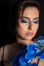 Portrait of young stunning woman with closed eyes, bright blue eyeshadows covering shoulder with branch of blue orchid.