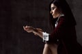 Portrait of young stylish woman brunette in black jacket and white shirt fastening he bracelet on her hand on grey Royalty Free Stock Photo