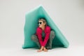 Portrait of young stylish girl in bright jacket and vintage pants posing, sitting under big paper piece isolated over Royalty Free Stock Photo