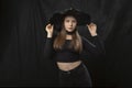 Portrait of young stylish girl in short tight-fitting top and wide-brimmed hat in the studio on black background. Young witch. Royalty Free Stock Photo