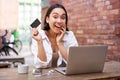 Portrait of young stylish girl sits near laptop, shows credit card and smiles, pays bills, shops online. Royalty Free Stock Photo