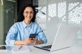 Portrait of young successful business woman at workplace inside office, female worker with phone in hands smiling and Royalty Free Stock Photo